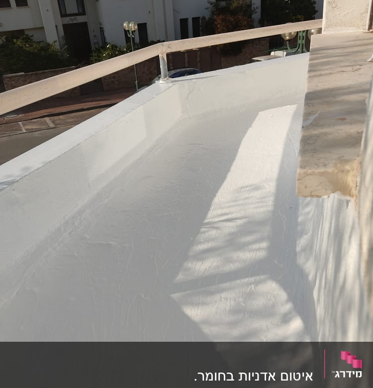 משטח אטום בלבן על גג עם מעקה מתכת